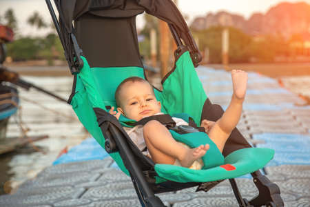 Happy one year old baby in a compact pram for traveling on the pier.