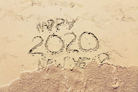 Inscription happy new 2020 on beach sand, wave covering text. New Year 2020 is coming concept.