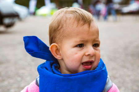 A small child with a blue bandana bandage around his neck. The kid screams to the side and calls someone.の写真素材