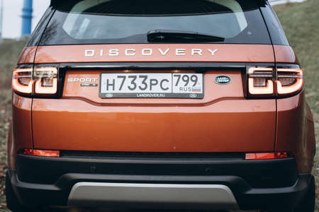 Moscow, Russia - December 20, 2019: Back side View of all new premium england suv. Land rover Discovery sport parked in the forest. Orange all wheel drive car standed on the ground.のeditorial素材