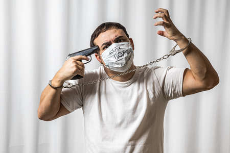 Depressed state. Suicide desire. The horror of isolation. The man in the mask. Handcuffed. With a pistol. Medical quarantine. Mental disorder. On a white background. Prisonerの写真素材
