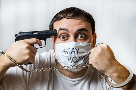 Depressed state. Suicide desire. The horror of isolation. The man in the mask. Handcuffed. With a pistol. Medical quarantine. Mental disorder. On a white background. Prisonerの写真素材