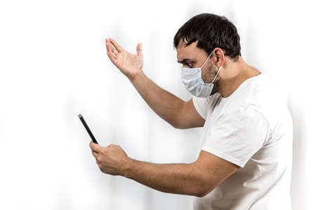 The man saw the bad news on his phone. Virus pandemic and epidemic. A man wearing a medical mask on his face.の写真素材