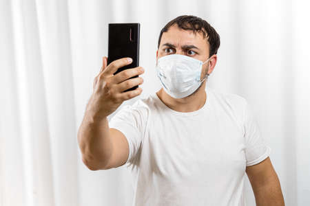 The man saw the bad news on his phone. Virus pandemic and epidemic. A man wearing a medical mask on his face.の写真素材