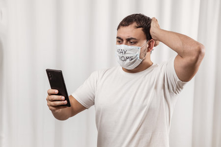 A man in a medical mask is playing a console. in the hands of a joystick. quarantine and isolation.の写真素材