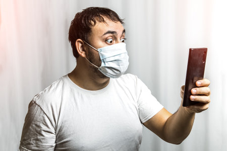 A man in panic looks at the phone and reads the news of the epidemic. In a protective medical maskの写真素材