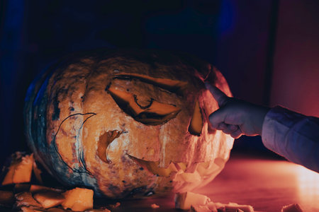 a child's hand points to a carved Halloween pumpkinの写真素材