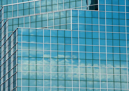 Reflection of a blue sky and clouds in the mirrored glass of a tall office building.