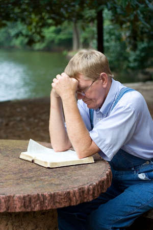 An older man praying by the lake.