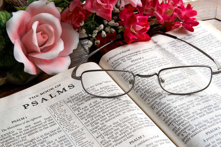 An open Bible with reading glasses lying on it and flowers in the background.の写真素材