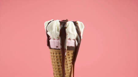 Vanilla ice cream with waffle cone and chocolate glaze close-up on pink background