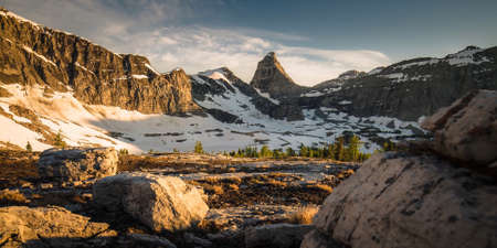 Mountain glade closed from all sides by high rocky mountains at the foot of which lies snowの写真素材