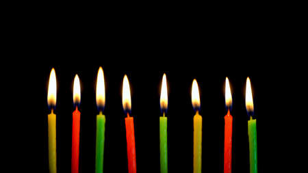 Festive thin colored candles are lit in the dark, lined up in a rowの写真素材