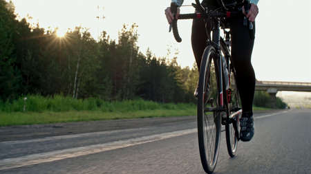 Cyclist rides on an asphalt road near a forest outside the city early in the morningの写真素材