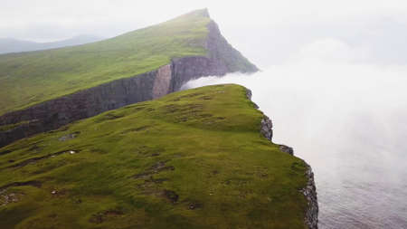 View from the top of the mountain over the ocean covered with grass and white cloudsの写真素材