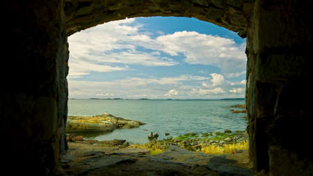 View of the shore of the bay in Helsinki through the archway between the stone walls, on a sunny dayの写真素材