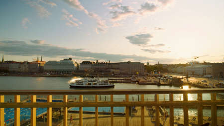 A view from the shore of a pleasure boat sailing to the pier in Helsinki at sunsetの写真素材