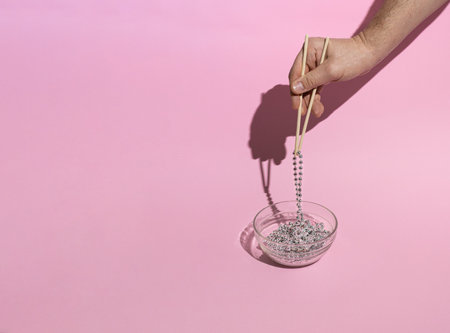 Bowl of shiny pearls, picked with chinese sticks. Minimal composition on pink background.の写真素材