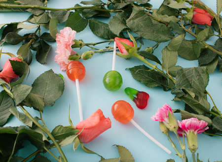 Romantic and playful composition with various flowers, Pink roses, lollipops, and candies on a pastel blue background. Creative arrangementの写真素材