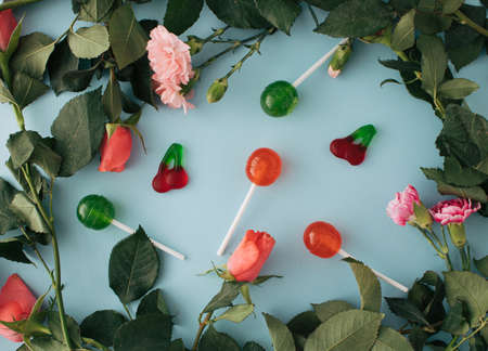 Romantic and playful composition with various flowers, Pink roses, lollipops, and candies on a pastel blue background. Creative arrangementの写真素材