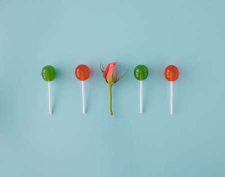 Lollipops, various colores, red and green in line with pink rose on pastel blue background. Be...