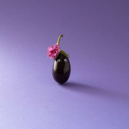 Girly look eggplant with pink autumn flower and eyes. Minimal creative funny concept on purple background.の写真素材