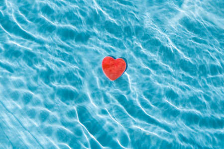 Red heart under the clear bright blue wavy water. Minimal Love , valentines concept.