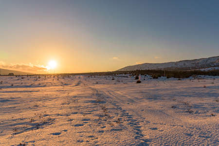 Amazing orange sunset in snow-covered field with footprints. Russia, Stary Krym.の写真素材