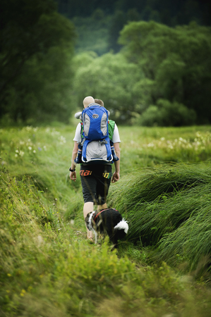 BOHEMIAN FOREST, CZECH REPUBLIC, August 2016: The Man Going through the Grass with Son in Baby Carrier. Dog Accompanies Them.のeditorial素材