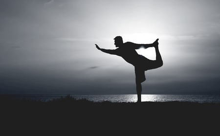 Silhouette of Young Man Practicing Yoga. Sunset on the Seacoast. Standing Bow Pose.の写真素材