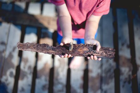 Child holding a selfmade simple boat from bark. Bloored mooded photo.
