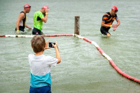 Germany, Ilshofen, Juny 2019: Child boy taking photos of competitors. The End of swimmen. Thriatlon.のeditorial素材