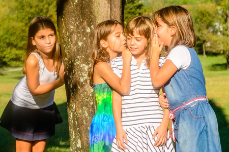 Four little girls playing and whispering in the parkの写真素材