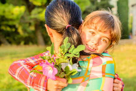 Mother and Daughter hugging. Daughter has brought her mother flowers.の写真素材