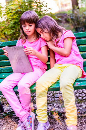 Two little girls are sitting on the bench in the park and readingの写真素材
