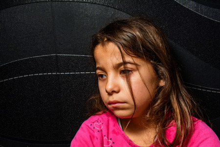Sad little girl is sitting in the corner of the roomの写真素材