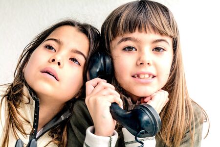 Seven year old girl talking on the old vintage phone and her sister eavesdropping her conversation. White background.の写真素材