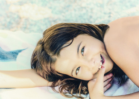 Adorable little girl laying on the sand and smilingの写真素材