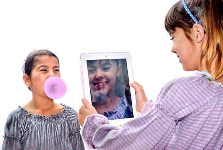 Beautiful little girl taking pictures with tablet of her sister blowing bubbles