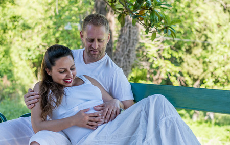 Pregnant woman flirting and hugging with her boyfriend in the parkの写真素材