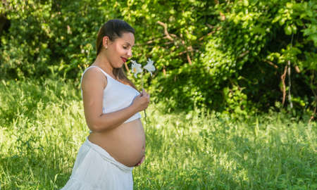 Young happy pregnant woman smelling flower in the parkの写真素材