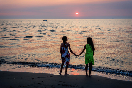 Two little girls walking together on the beach in the sunsetの写真素材