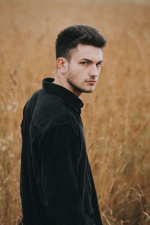 A young handsome guy with a small beard in a black shirt looks at the cameraの写真素材