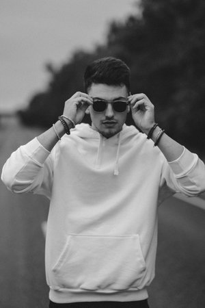 A young handsome guy with a small beard in a white jacket and dark glasses is walking along the road. Black and whiteの写真素材