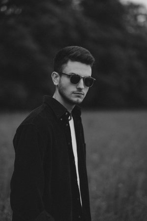 A young handsome guy with a small beard in a black shirt and dark glasses looks at the camera. Black and whiteの写真素材