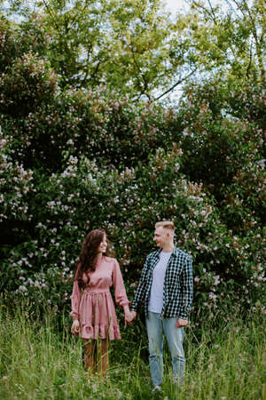 Young couple, a guy and a girl, stand near a flowering bush and look at each otherの写真素材