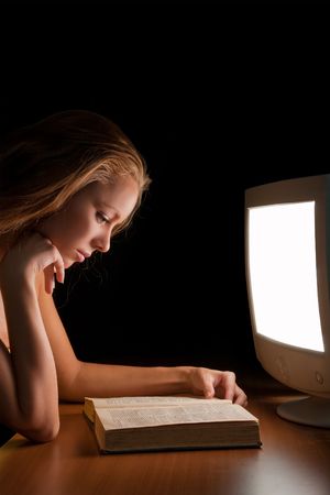 girl reading a book (textbook) in the light of a working computerの写真素材