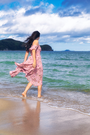 Young woman walking on sandy beach in a long colorful dressの写真素材