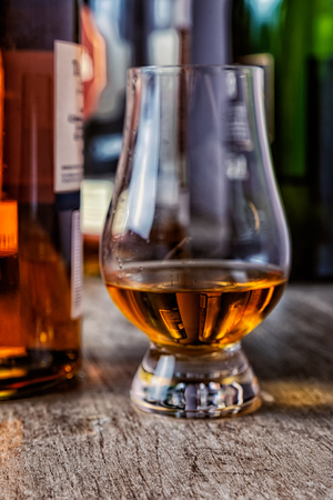 Whisky glass with single malt scotch on wooden table and scotch bottles on the backgroundの写真素材