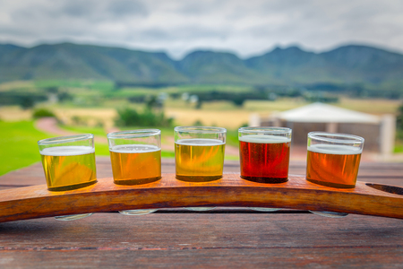 Beer tasting glasses on a wooden tray outside the brewery with a beautiful view of the mountains in South Africaの写真素材